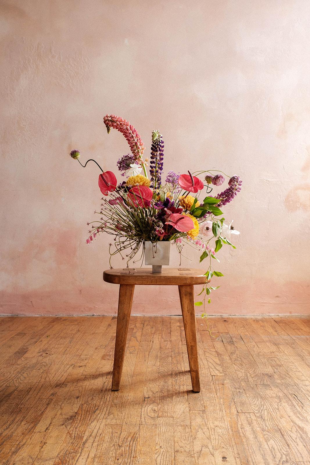 A lush seasonal arrangement gathered loose on a wood stool
